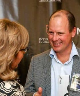 Man in a checkered blazer conversing with a woman at a formal event. - Olive Oil Times