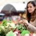 Woman examining fresh vegetables at a market stall with various produce visible. - Olive Oil Times