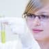 Woman wearing glasses and a lab coat holding a test tube with yellow liquid in a laboratory setting. - Olive Oil Times