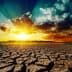 Dry, cracked earth with a vibrant sunrise and clouds in the background. - Olive Oil Times
