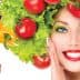 Woman with a hairstyle made of lettuce and tomatoes, smiling and posing with a hand on her face. - Olive Oil Times
