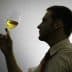 Silhouette of a person holding a glass of yellow liquid, examining it with a thoughtful expression. - Olive Oil Times
