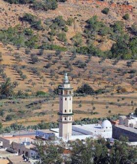 A tall minaret located in a rural area with olive trees in the background. - Olive Oil Times