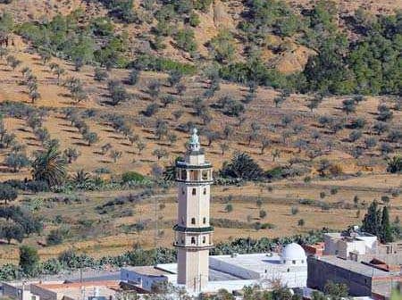 A tall minaret located in a rural area with olive trees in the background. - Olive Oil Times