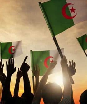 People holding Algerian flags with raised hands against a sunset background. - Olive Oil Times