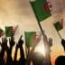 People holding Algerian flags with raised hands against a sunset background. - Olive Oil Times
