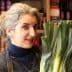 Woman with gray hair holding a bunch of fresh leeks in a market setting. - Olive Oil Times