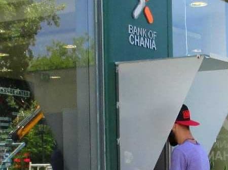 Person using an ATM at the Bank of Chania with a visible bank logo. - Olive Oil Times