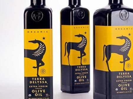 Three bottles of Terra Delyssa organic extra virgin olive oil with a yellow label featuring a black horse design. - Olive Oil Times