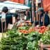 Vegetable market with various fresh produce including greens, tomatoes, and herbs displayed on wooden crates. - Olive Oil Times