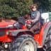 A woman wearing sunglasses and a striped shirt sitting on a red tractor, holding a tool. - Olive Oil Times