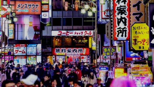 Busy street in Tokyo filled with people and illuminated neon signs in various colors and languages. - Olive Oil Times