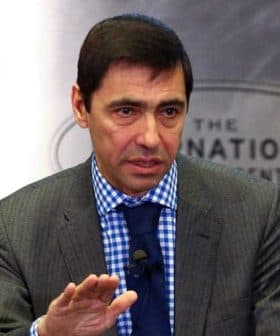 Man in a gray suit with a blue checkered shirt speaking during an event at the National Center. - Olive Oil Times