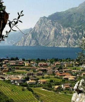 A scenic view of Lake Garda featuring mountains and a village with terracotta-roofed buildings. - Olive Oil Times
