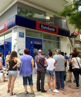 Customers waiting in line outside a Eurobank branch in a city setting. - Olive Oil Times