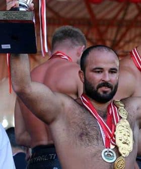 Athlete celebrating victory by holding a trophy and wearing multiple medals at a competition. - Olive Oil Times