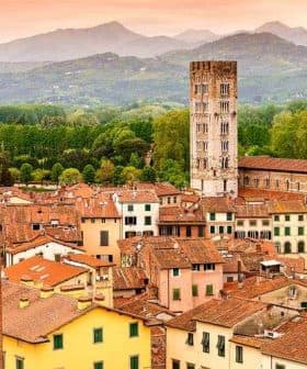 Aerial view of Lucca's rooftops featuring a historic tower and surrounding mountains. - Olive Oil Times