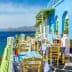 Outdoor dining area featuring tables and chairs in front of a blue and green building by the sea. - Olive Oil Times