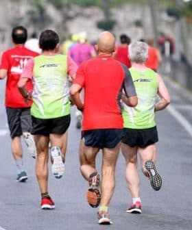 Three runners wearing colorful athletic clothing jogging on a road during a running event. - Olive Oil Times