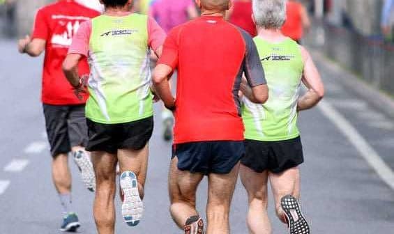Three runners wearing colorful athletic clothing jogging on a road during a running event. - Olive Oil Times