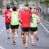 Three runners wearing colorful athletic clothing jogging on a road during a running event. - Olive Oil Times