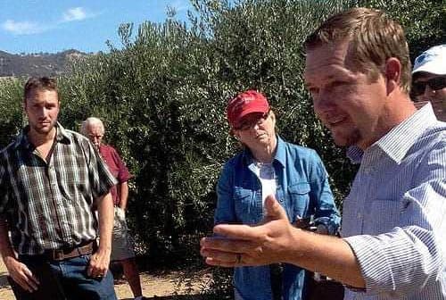 A group of people gathered in an olive grove, with one person speaking to the others. - Olive Oil Times