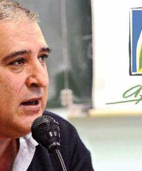 A man speaking into a microphone at a conference with a logo visible in the background. - Olive Oil Times