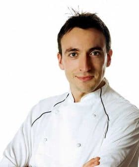 A chef wearing a white uniform with arms crossed, looking directly at the camera. - Olive Oil Times