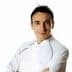 A chef wearing a white uniform with arms crossed, looking directly at the camera. - Olive Oil Times