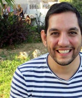Man with short dark hair wearing a striped shirt, smiling at the camera outdoors. - Olive Oil Times