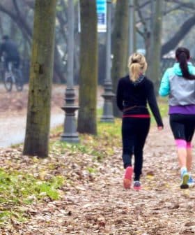 Two women jogging on a path lined with trees in a park during autumn. - Olive Oil Times