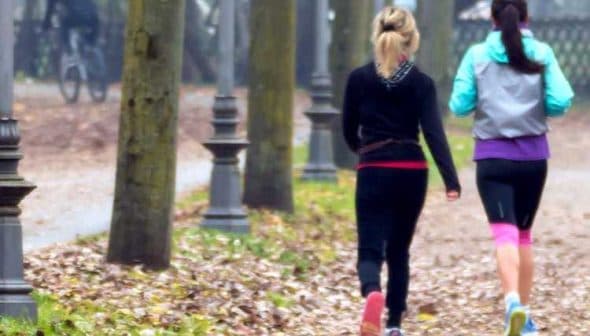 Two women jogging on a path lined with trees in a park during autumn. - Olive Oil Times