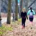 Two women jogging on a path lined with trees in a park during autumn. - Olive Oil Times
