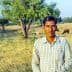 A man in a checked shirt stands in a field with cattle grazing in the background. - Olive Oil Times