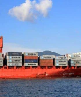 Red cargo ship loaded with shipping containers, including Maersk branding, on the water. - Olive Oil Times