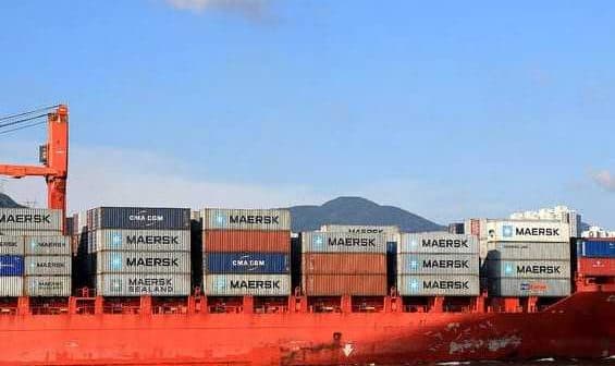 Red cargo ship loaded with shipping containers, including Maersk branding, on the water. - Olive Oil Times