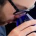 Individual wearing glasses bringing a blue glass close to their face for smelling. - Olive Oil Times