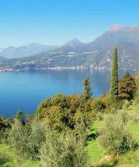 A scenic view of a lake surrounded by mountains and trees under a clear blue sky. - Olive Oil Times