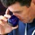 Man holding a blue glass cup and smelling the contents while tasting olive oil. - Olive Oil Times
