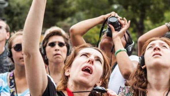 A group of tourists looking up at a landmark while wearing headphones and holding cameras. - Olive Oil Times