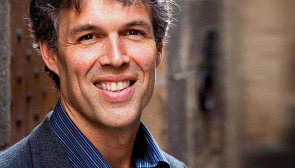 A man with gray hair and a suit smiling at the camera in an outdoor setting. - Olive Oil Times