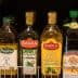 Various bottles of extra virgin olive oil, including Sagra and Fragata brands, displayed on a shelf. - Olive Oil Times