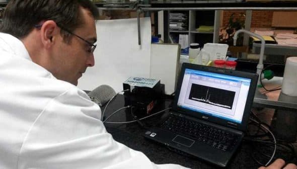 A scientist in a lab coat examining data displayed on a laptop screen in a laboratory setting. - Olive Oil Times