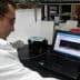 A scientist in a lab coat examining data displayed on a laptop screen in a laboratory setting. - Olive Oil Times