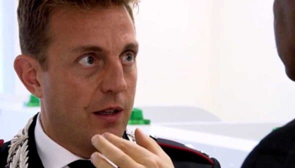 A man in a formal uniform with a decorative collar engaged in conversation with another individual. - Olive Oil Times