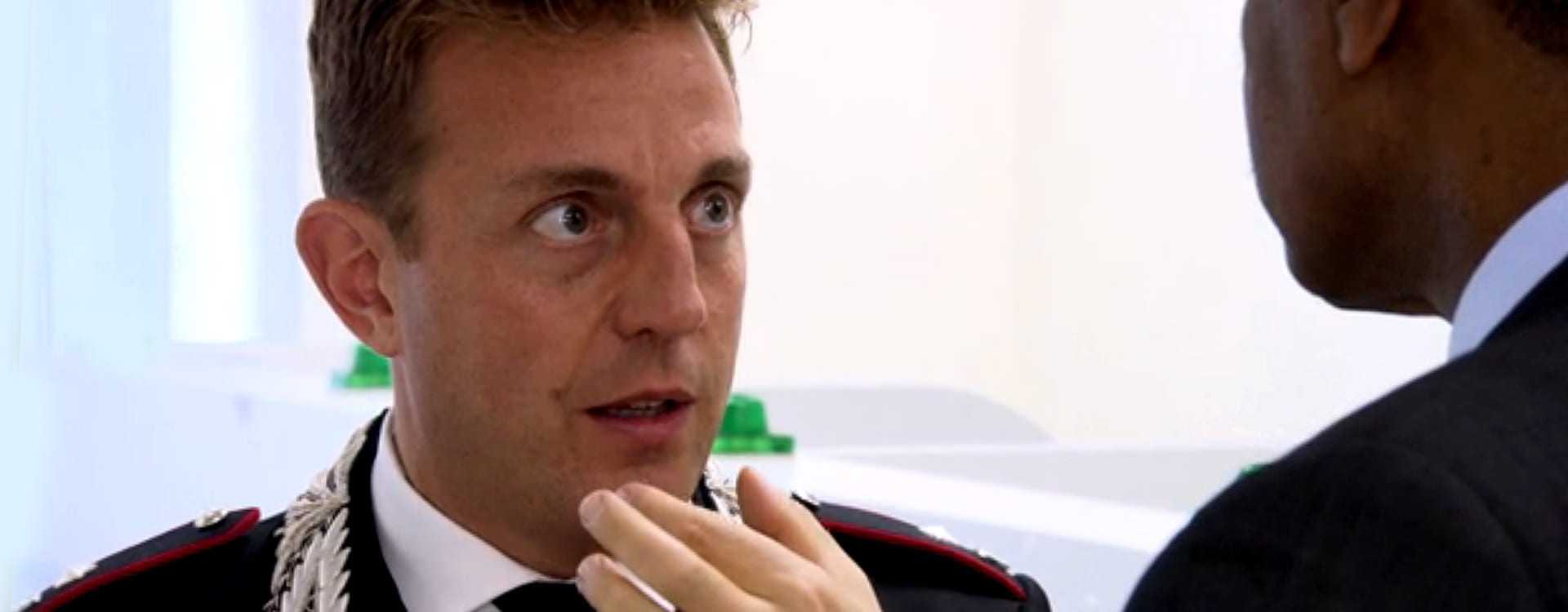 A man in a formal uniform with a decorative collar engaged in conversation with another individual. - Olive Oil Times