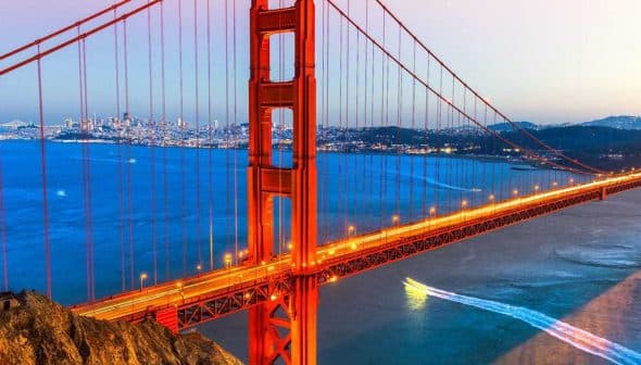 Golden Gate Bridge illuminated at sunset with a city skyline in the background. - Olive Oil Times