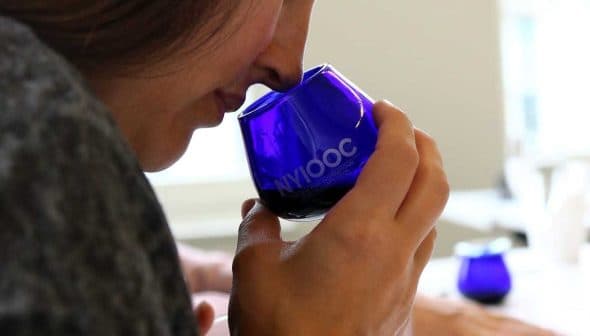 Individual holding a blue glass cup while smelling olive oil during a tasting session. - Olive Oil Times
