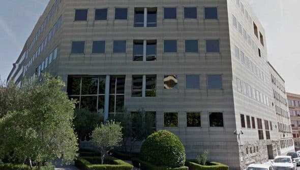 Contemporary office building featuring large glass windows and a landscaped area. - Olive Oil Times