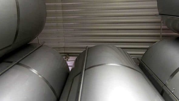 Stacked metal storage tanks in a warehouse with a metallic finish and cylindrical shape. - Olive Oil Times